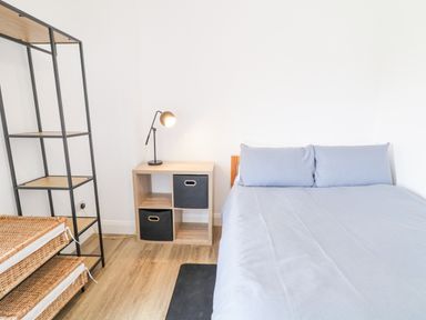A bedroom with a bed with blue bedding a wooden nightstand with storage bins and a lamp a black metal shelving unit and a wicker basket on a wooden floor at Ballyness Bay in Killult Upper near Gortahork County Donegal