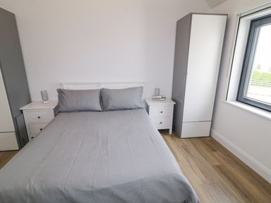 A bedroom with a bed dressed in gray sheets between two white nightstands and gray and white wardrobes near a window at Ballyness Bay in Killult Upper near Gortahork County Donegal