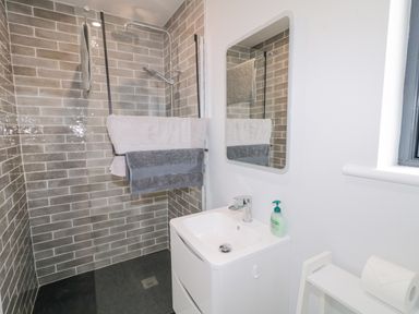 A bathroom with a walk-in shower, two towels on a rail, a sink with a soap dispenser, a mirror, a window, and a toilet paper holder at Ballyness Bay in Killult Upper near Gortahork County Donegal