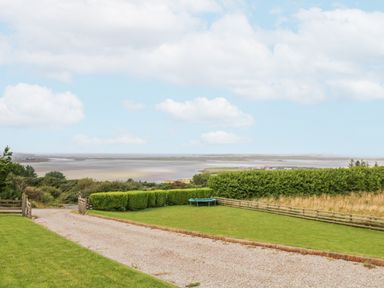 A gravel driveway and grass lawn with a trampoline and hedges overlooking a body of water at Ballyness Bay in Killult Upper near Gortahork County Donegal