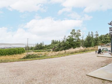 A gravel driveway with chairs and a picnic table near a stone building overlooking grassy fields and trees at Ballyness Bay in Killult Upper near Gortahork County Donegal