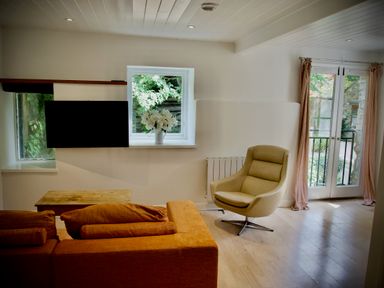 A living room with an orange sofa a beige armchair a wooden coffee table and flowers on a windowsill at Windrush in Burford