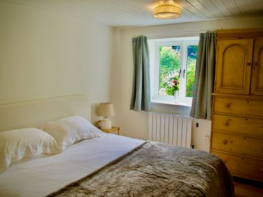 A bedroom with a double bed bedside table with lamp window with curtains and a wooden wardrobe at Windrush in Burford
