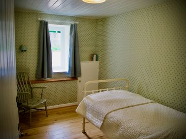 A bedroom with a single bed a wooden chair and a window with curtains at Windrush in Burford