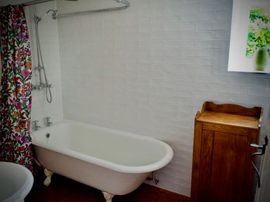 A bathroom with a clawfoot bathtub floral shower curtain and a wooden cabinet at Windrush in Burford