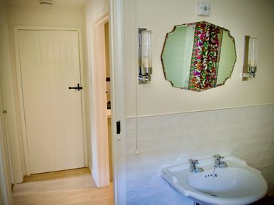 A bathroom with a sink a mirror two wall lights and a door with a latch at Windrush in Burford
