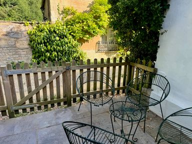 A small patio area with three metal chairs and a wooden fence surrounded by plants at Windrush in Burford