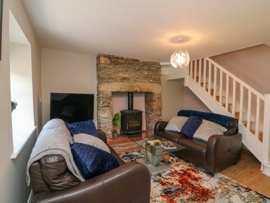 A living room with two brown sofas a glass coffee table a stone fireplace and a staircase at An Teach Ban in Bunclody County Wexford