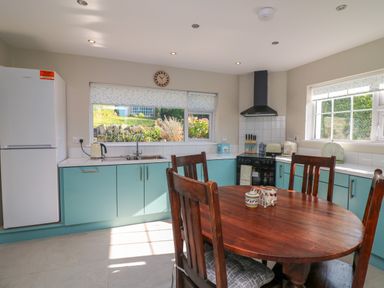 A kitchen with wooden dining table and chairs teal cabinets white refrigerator and large windows at An Teach Ban in Bunclody County Wexford