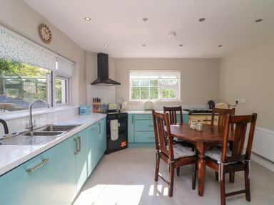 A kitchen with blue cabinets a black stove a wooden dining table with four chairs and two windows at An Teach Ban in Bunclody County Wexford