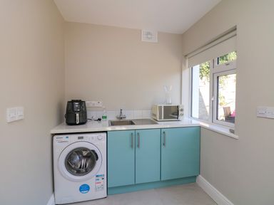 A utility room with a washing machine a sink cabinets an air fryer microwave and a window at An Teach Ban in Bunclody County Wexford