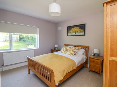 A bedroom with a wooden bed and matching bedside tables by a window and a wardrobe at An Teach Ban in Bunclody County Wexford