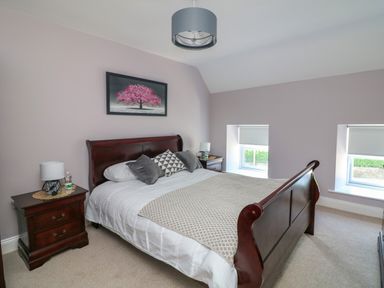 A bedroom with a wooden bed frame white bedding two windows and bedside tables at An Teach Ban in Bunclody County Wexford