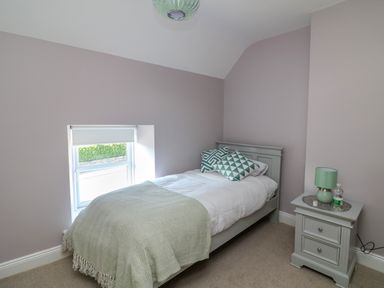 A bedroom with a single bed, bedside table with lamp and bottle, and a window with a blind at An Teach Ban in Bunclody County Wexford