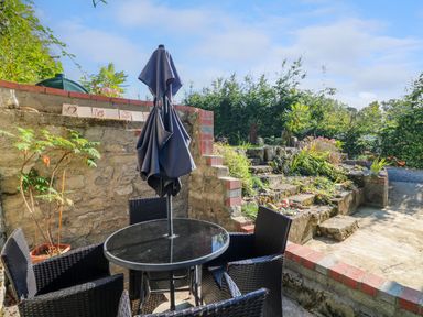 An outdoor patio area with a round glass table four black wicker chairs and a closed umbrella at An Teach Ban in Bunclody County Wexford