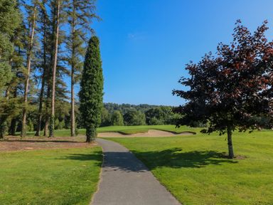 A golf course with a sand bunker trees and a paved pathway at An Teach Ban in Bunclody County Wexford