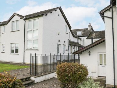 An exterior view of white residential buildings with multiple windows a black metal railing and a paved walkway at Ramblers Lodge in Bowland Bridge near Bowness-On-Windermere Lake District