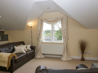 A living room with leather sofas floor lamp patterned curtains and a window at Ramblers Lodge in Bowland Bridge near Bowness-On-Windermere Lake District