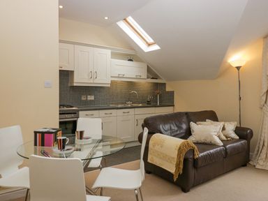 A kitchen and dining area with a glass table and white chairs and a brown leather sofa with cushions near a floor lamp at Ramblers Lodge Bowland Bridge near Bowness-On-Windermere Lake District