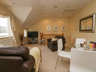 A living room with brown leather chairs a glass dining table and a television at Ramblers Lodge in Bowland Bridge near Bowness-On-Windermere Lake District