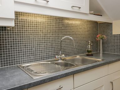 A kitchen sink with a faucet and a bottle next to a vase with flowers at Ramblers Lodge Bowland Bridge near Bowness-On-Windermere Lake District