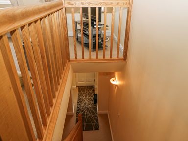 A staircase with wooden railings leading down to a hallway with a patterned runner and a closed door at Ramblers Lodge Bowland Bridge near Bowness On Windermere Lake District