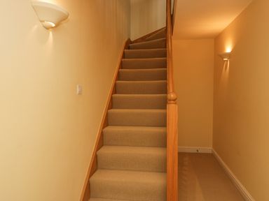 A staircase with carpet and wooden handrail in a hallway with wall lights at Ramblers Lodge Bowland Bridge near Bowness-On-Windermere Lake District