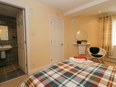 A bedroom with a bed covered in plaid bedding folded towels on the bed an open door to a bathroom a round mirror above a small white shelf a chair and a window with curtains at Ramblers Lodge Bowland Bridge near Bowness-On-Windermere Lake District