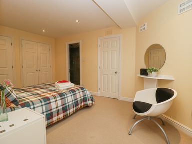 A bedroom with a bed covered in checkered bedding, a chair, a small wall shelf with a round mirror, and three closed doors at Ramblers Lodge Bowland Bridge near Bowness-On-Windermere Lake District