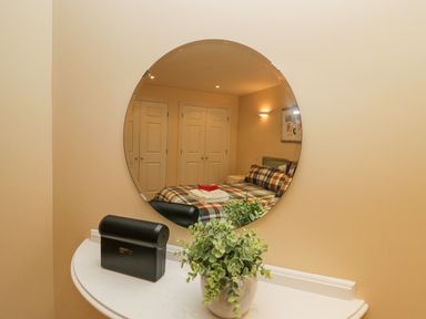 A round mirror reflecting a bedroom with a bed with plaid bedding towels on the bed and closet doors at Ramblers Lodge in Bowland Bridge near Bowness-On-Windermere Lake District