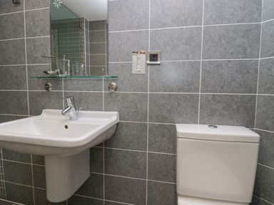 A bathroom with a white wall-mounted sink and a white toilet against gray tiled walls at Ramblers Lodge in Bowland Bridge near Bowness-On-Windermere Lake District