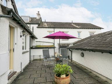 An outdoor patio with two chairs a table with a purple umbrella and a potted plant at Ramblers Lodge in Bowland Bridge near Bowness-On-Windermere Lake District