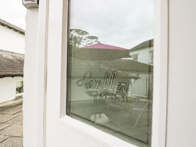 Close up of a glass door with Ramblers Lodge written on it and outdoor patio furniture and umbrella reflected in the glass at Ramblers Lodge in Bowland Bridge near Bowness-On-Windermere Lake District