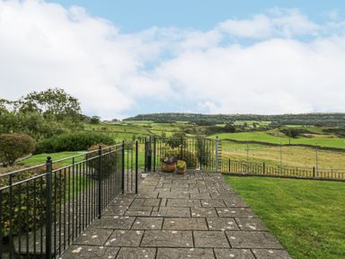 A paved patio with metal railings and potted plants overlooking green fields and hills at Ramblers Lodge Bowland Bridge near Bowness-On-Windermere Lake District