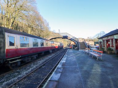 Train platform with benches a footbridge and a brick building at a rural station