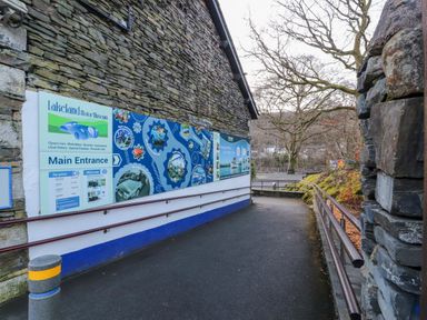 An outdoor ramp leading to the main entrance of Lakeland Motor Museum with a large sign on a stone wall and trees in the background at Ramblers Lodge in Bowland Bridge near Bowness-On-Windermere Lake District