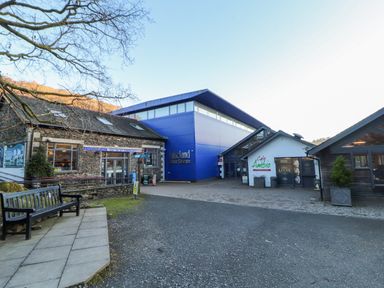 An outdoor view of the Lakeland Motor Museum and Cafe Ambio with stone and modern buildings and a bench nearby