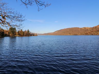A lake with hills and trees in the background under a clear blue sky at Ramblers Lodge in Bowland Bridge near Bowness-On-Windermere Lake District