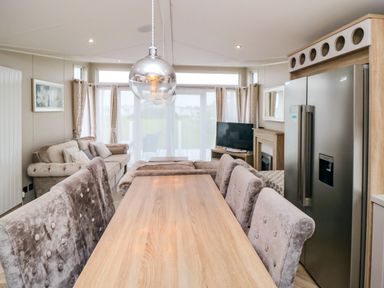 A dining table with upholstered chairs a sofa a television and a refrigerator in a living room at Finch 65 in Cayton Bay