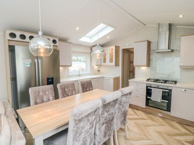 A kitchen with a wooden dining table and upholstered chairs a stainless steel refrigerator a gas stove and overhead lighting at Finch 65 in Cayton Bay