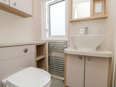 A bathroom with a toilet a sink with cabinet a towel radiator and a frosted window at Finch 65 in Cayton Bay