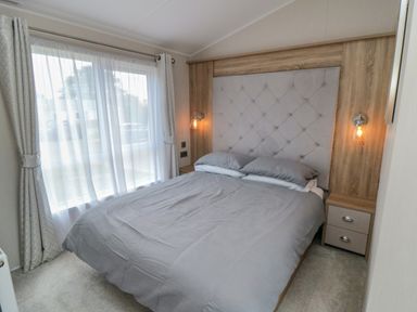 A bedroom with a bed with headboard bedside tables and lamps next to a window with curtains at Finch 65 in Cayton Bay