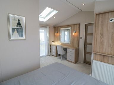 A bedroom with a bed, desk with chair, mirror, wall lights, window with curtains and a framed picture on the wall at Finch 65 in Cayton Bay