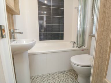 A bathroom with a pedestal sink a bathtub with shower screen a toilet and patterned floor tiles at Finch 65 in Cayton Bay