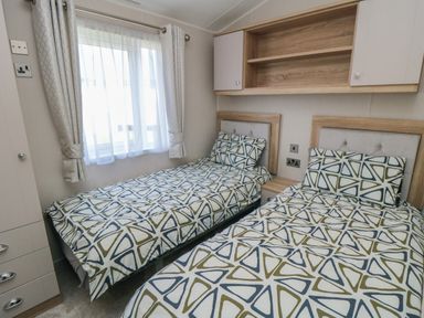 A bedroom with two single beds with patterned bedding and a window with curtains at Finch 65 in Cayton Bay