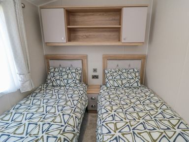 A bedroom with two single beds with geometric patterned bedding and a wooden shelf above at Finch 65 in Cayton Bay