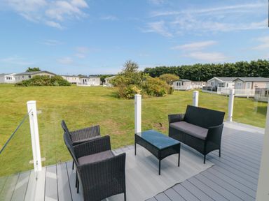 A deck with outdoor wicker furniture including two chairs a loveseat and a coffee table overlooking a grassy area with homes at Finch 65 in Cayton Bay