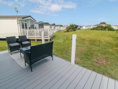 A patio with black chairs and a table overlooking grass and several mobile homes at Finch 65 in Cayton Bay