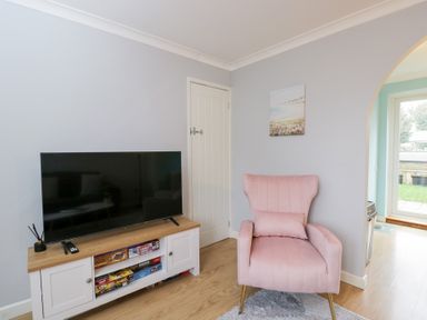 A living room with a television and a pink chair at 20 Honeycroft in Bourton-On-The-Water