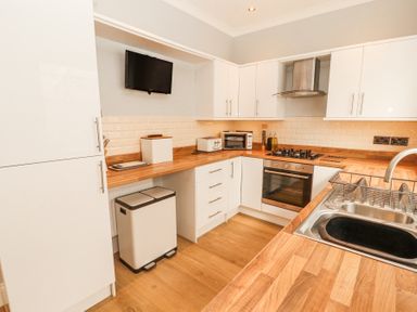 A kitchen with white cabinets wooden countertops a stainless steel sink gas stove oven toaster and mounted television at Grace House in Silloth